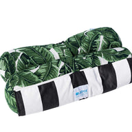 This decorative pillow showcases green banana leaves on one side and black and white stripes on the other. Made from marine-grade fabric, its ideal for outdoor use. The blue Ledge Lounger label is visible at its rectangular edge, perfect for your Laze Hammock or patio chair.