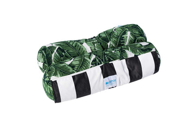 This decorative pillow showcases green banana leaves on one side and black and white stripes on the other. Made from marine-grade fabric, its ideal for outdoor use. The blue Ledge Lounger label is visible at its rectangular edge, perfect for your Laze Hammock or patio chair.