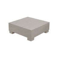 The Signature Coffee Table by Ledge Lounger is a square, grey stone pedestal with four short feet, making it an elegant piece perfect for complementing your poolside essentials against a pristine white backdrop.