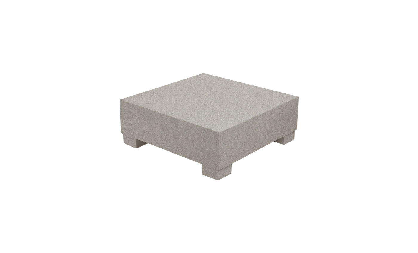 The Signature Coffee Table by Ledge Lounger is a square, grey stone pedestal with four short feet, making it an elegant piece perfect for complementing your poolside essentials against a pristine white backdrop.