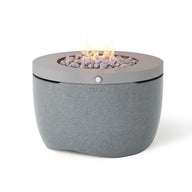 The Halo Firepit by Ledge Lounger is a round, modern propane fire pit featuring a smooth stone-like base and metal top. Filled with decorative stones and visible flames, it creates the perfect outdoor ambiance against a plain white background.