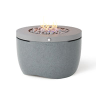 The Halo Firepit by Ledge Lounger is a modern propane fire pit with a pivot-glide lid. It features a smooth, cylindrical stone-like base and circular metal top, small stones, and visible flames designed to enhance your outdoor ambiance.