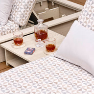 Two patterned lounge chairs with triangle designs, each topped with a white pillow. The Echo Side Table by Ledge Lounger holds a decanter, two glasses filled with amber liquid, and a deck of cards on a wooden deck.