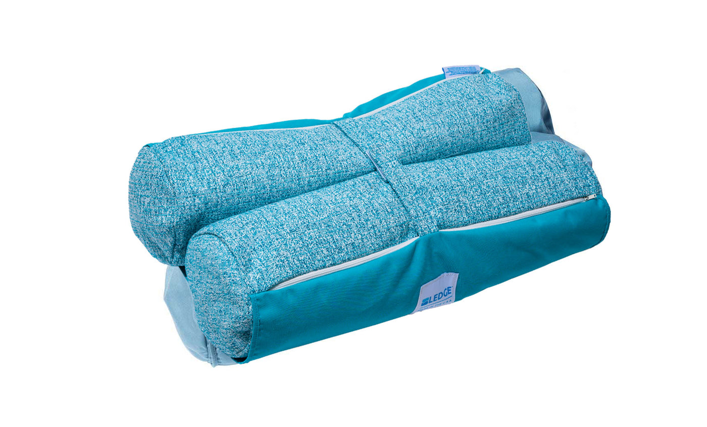 The Laze Hammock by Ledge Lounger is shown in turquoise with marine-grade fabrics. It has a textured finish, zippered pocket, and soft handle for easy carrying. Its compact design highlights functionality as it seamlessly blends into outdoor adventures while being neatly folded.