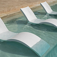 Three Ledge Lounger Outdoor Oasis In-Pool Furniture Deep Chaises are partially submerged in the clear, shallow pool, perfectly aligned for sunbathing in cool water. A stone tile edge frames this relaxing pool ledge scene.