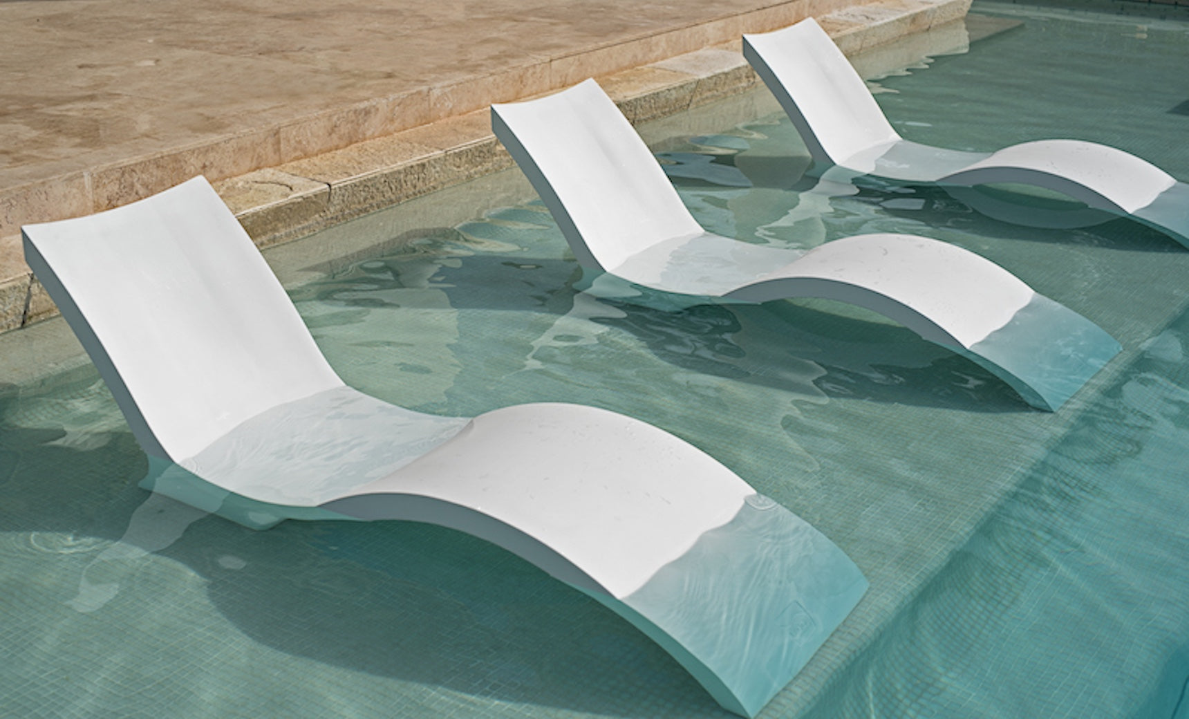 Three Ledge Lounger Outdoor Oasis In-Pool Furniture Deep Chaises are partially submerged in the clear, shallow pool, perfectly aligned for sunbathing in cool water. A stone tile edge frames this relaxing pool ledge scene.
