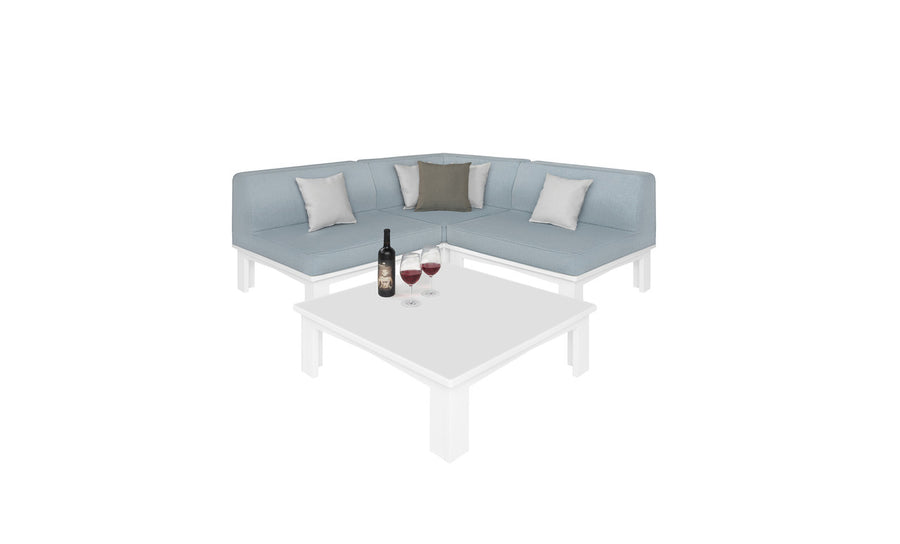 The Mainstay Sectional 4 Piece Diamond from Ledge Lounger in light blue forms a cozy corner with four cushions around a white square coffee table. The table features a wine bottle and two filled glasses, all set against a plain white background.