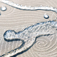 Close-up of clear water droplets on the beige spiral-patterned, waterproof fabric of the Ledge Lounger Laze Pillow, an outdoor comfort accessory. The droplets showcase the texture and water-repellent properties of this floating pool cushion.