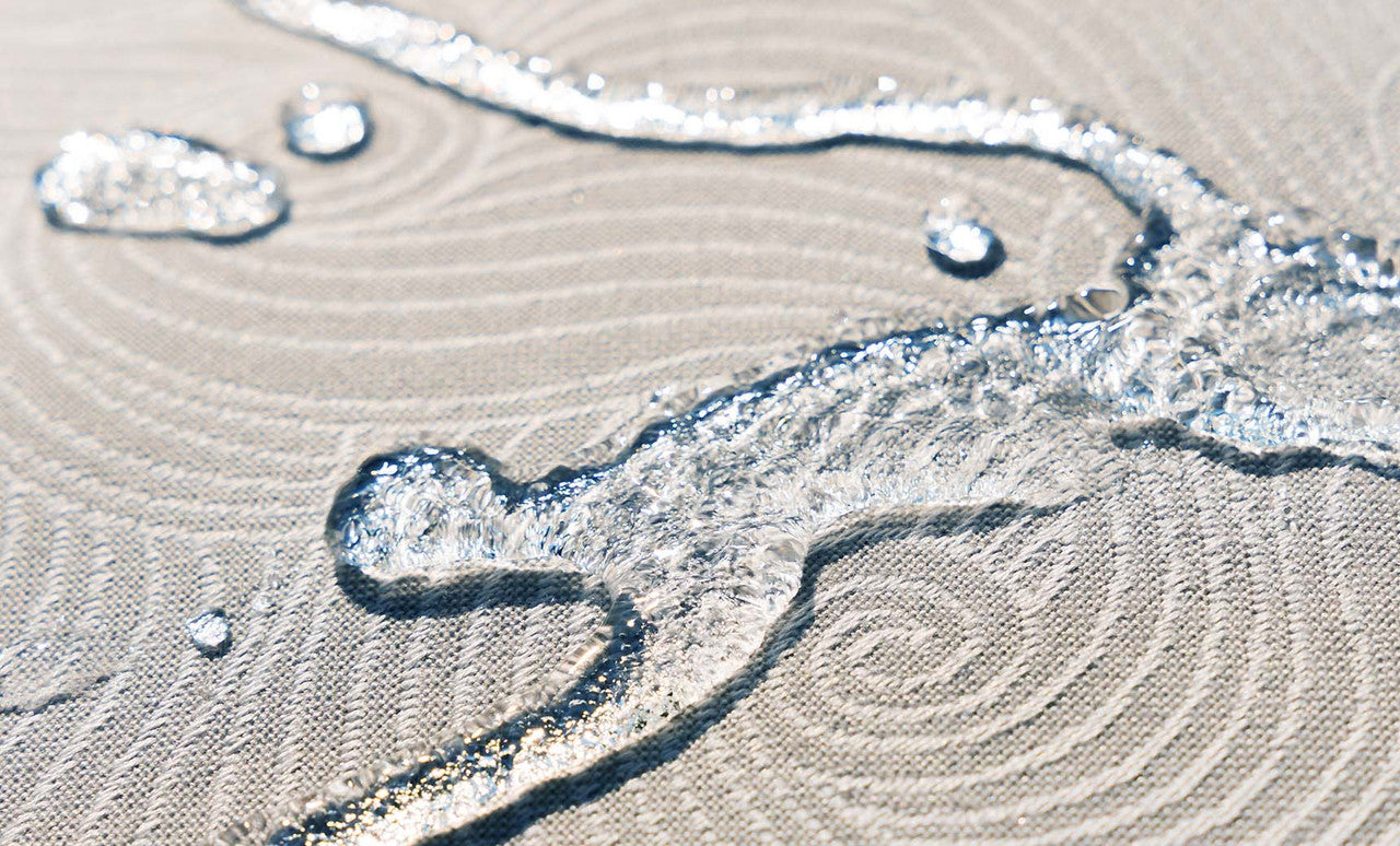 Close-up of clear water droplets on the beige spiral-patterned, waterproof fabric of the Ledge Lounger Laze Pillow, an outdoor comfort accessory. The droplets showcase the texture and water-repellent properties of this floating pool cushion.