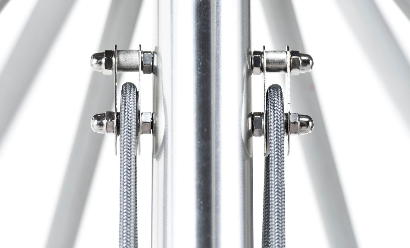 A close-up of a symmetrical metal structure with fiberglass ribs and vertical cables flanking a central pole mirrors the industrial aesthetic of an Essential Fiberglass Umbrella - 10 Square Pulley by Ledge Lounger against a bright white backdrop.