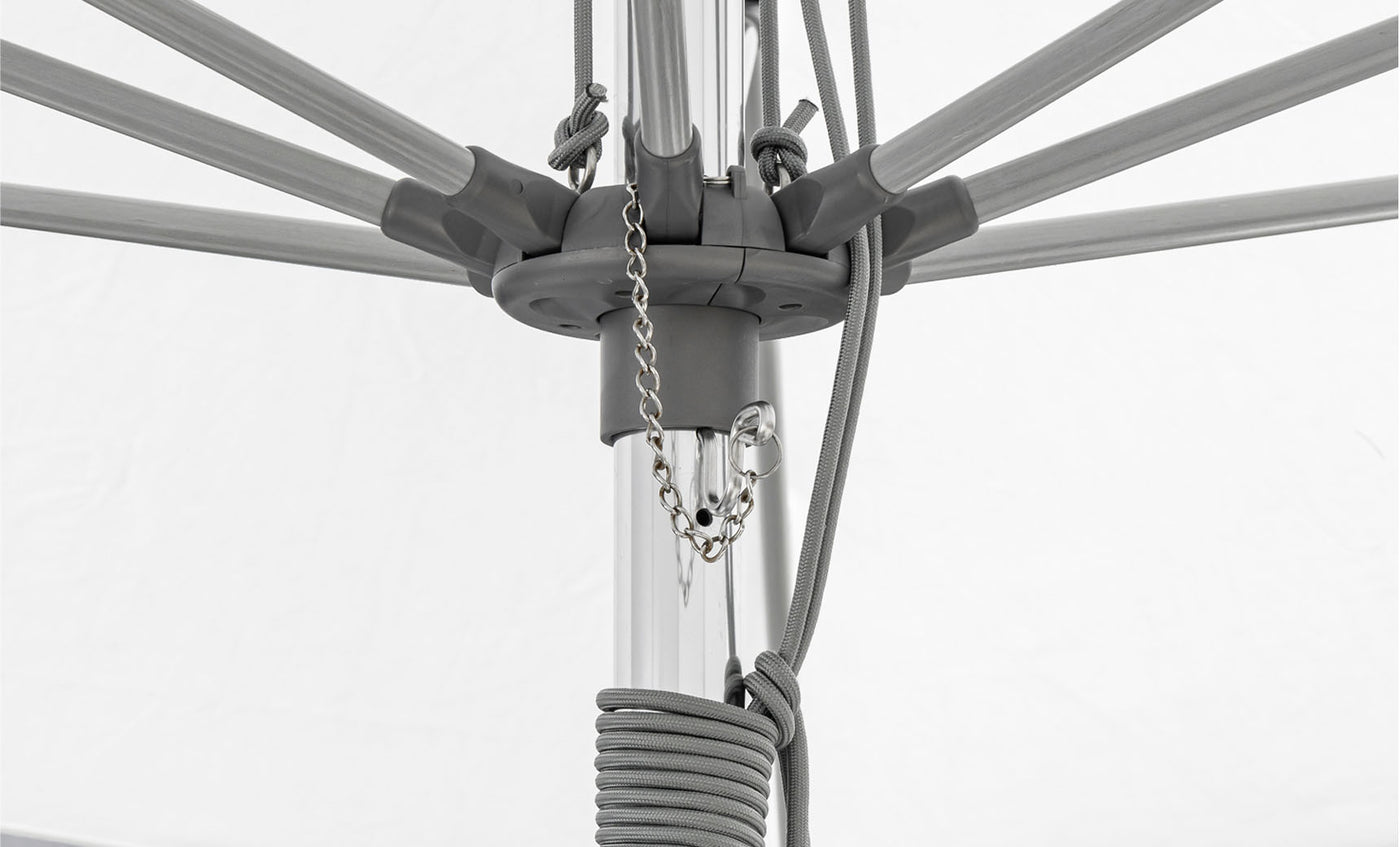 Close-up of the 10 Square Essential Fiberglass Umbrella by Ledge Lounger, highlighting its central pole with extending spokes. Chains and ropes attach to the pole, with cords wrapped around it. Marine-grade fabrics ensure durability against a white background.