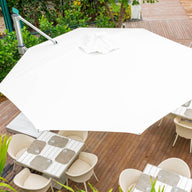 The Ultra Cantilever Umbrella - 10 Square by Ledge Lounger, featuring a rechargeable umbrella light, shelters several square tables and chairs on a wooden deck, surrounded by lush greenery and a manicured lawn for a serene relaxation oasis.
