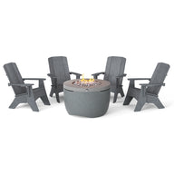 The Halo Aglow Bundle by Ledge Lounger features four dark gray Adirondack chairs around a round gray outdoor gas fire pit, embellished with small stones and a gentle central flame, set against a plain white background.