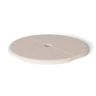 A beige, round ceramic saucer with a central hole and subtle grooves resembles the Ledge Loungers Signature Side Table Lid with Umbrella Hole. Displayed on a plain white background, it features a smooth surface and slightly raised edges, adding elegance to any poolside collection.