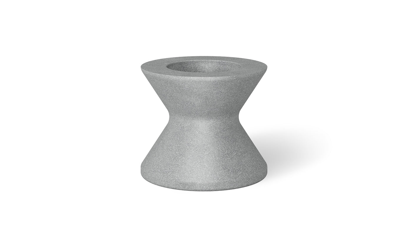 A small, hourglass-shaped gray object with a hollow top resembles an umbrella base. Its smooth surface and symmetrical design remind one of an industrial component. Shadows imply placement on a light surface, akin to the Signature Tall Ice Bin Side Table by Ledge Lounger.