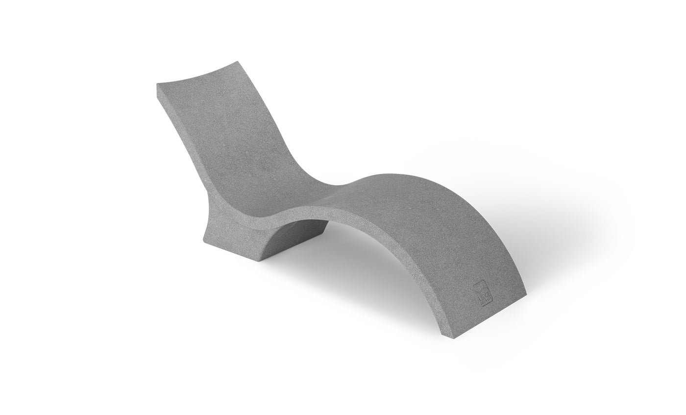 The Signature Chaise Deep by Ledge Lounger is a minimalist grey lounge chair with a wavy, modern design like a chaise lounge, featuring smooth surfaces and continuous curves for a sleek look. Its shown against a plain white background.