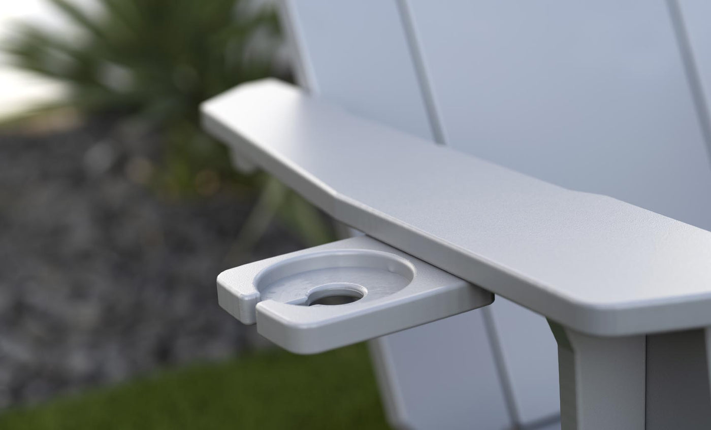 Close-up of the Mainstay Ultimate Adirondack by Ledge Lounger, a light gray outdoor lounge chair with a built-in cup holder. The blurred background of greenery and stones creates the perfect poolside relaxation setting.