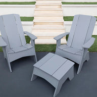 Two gray Ledge Lounger Adirondack chairs on a dark patio, showcasing durability and style, with a Mainstay Adirondack Ottoman in between. Background steps and grass patches complete the cozy outdoor setting.