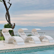 Three Ledge Lounger Signature Chaise Shades are arranged on a poolside patio, overlooking serene ocean waters. A solitary tree and lush greenery enhance the background, with clouds touching distant mountains at the horizon.