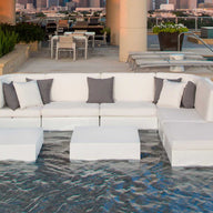 A modern outdoor lounge features a white sectional set and Ledge Loungers Signature Coffee Table in a shallow pool. A dining table with chairs against the skyline backdrop offers an exquisite view, highlighting our Signature Collection.