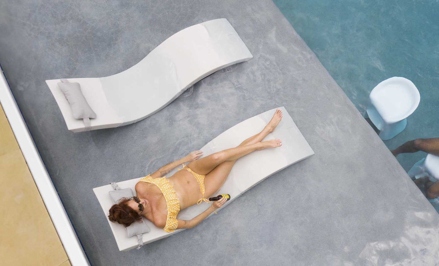 Friends in the backyard pool lounging on chaise and chatting on barstools.