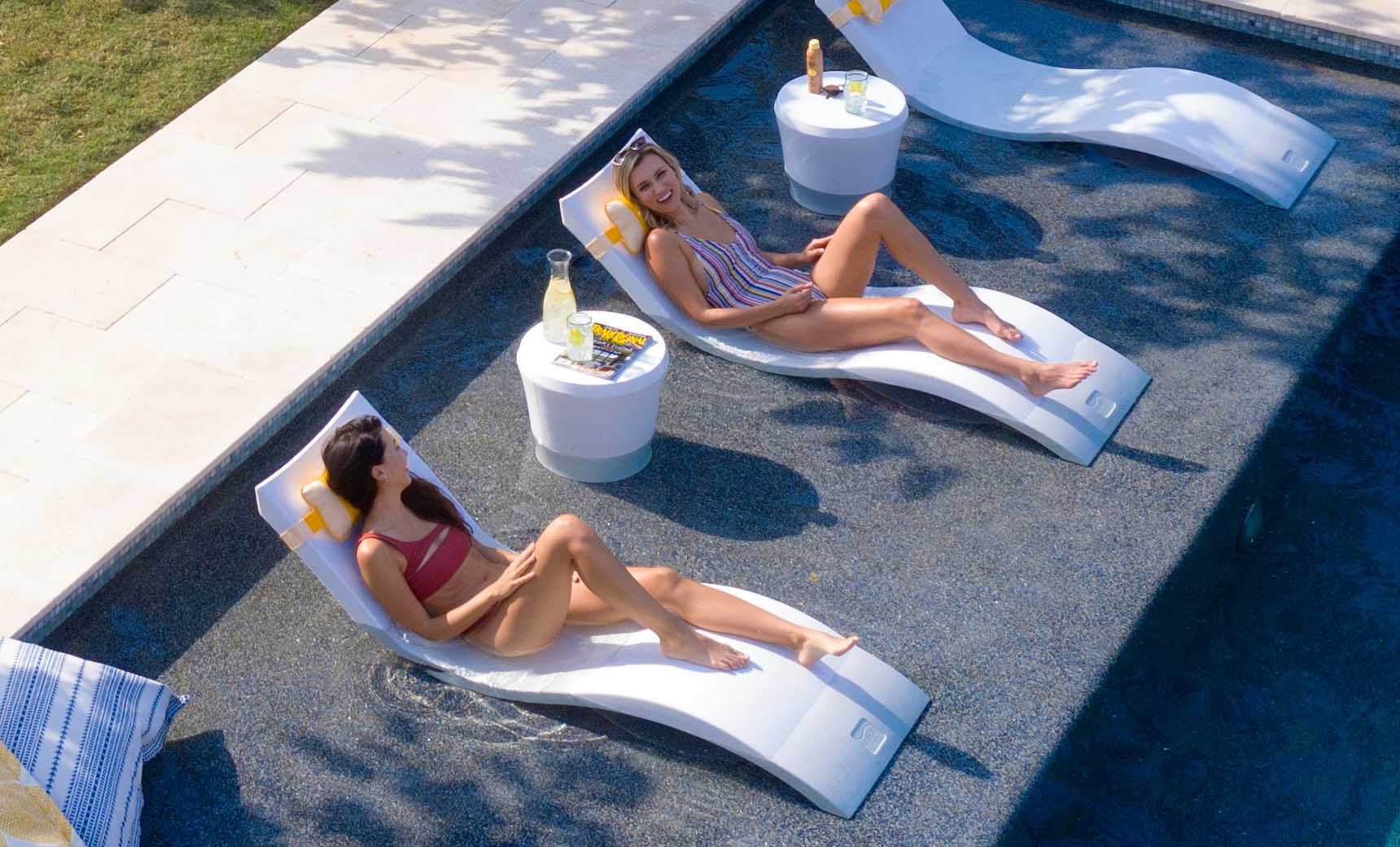 Girls smiling on in pool chaise loungers with matching headrest pillow and a side table.