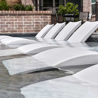 A row of signature chaises in white by ledge lounger in an apartment pool.