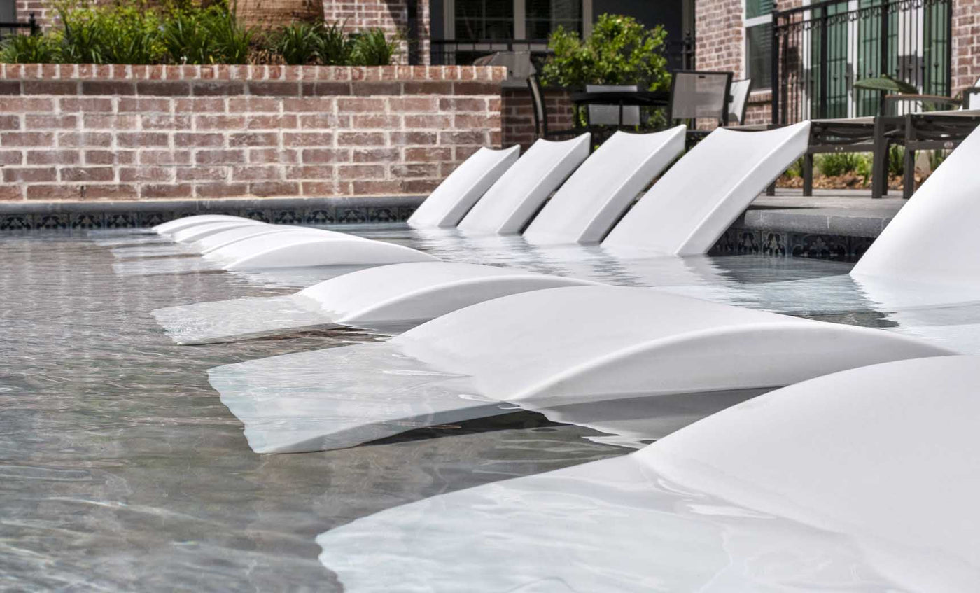 A row of signature chaises in white by ledge lounger in an apartment pool.