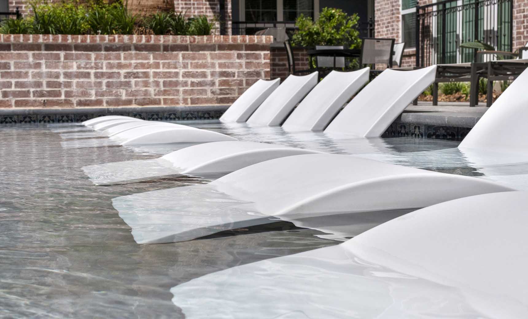 A row of signature chaises in white by ledge lounger in an apartment pool.