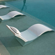 Three Ledge Lounger Signature Chaise Deep chairs, in modern white, are on a pool tanning ledge. Perfectly positioned, they invite relaxation as water gently laps over them, enhancing the area’s luxurious and tranquil ambiance.
