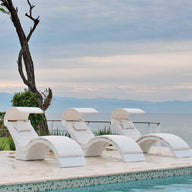 Three Signature Chaise Deep lounges by Ledge Lounger sit poolside, overlooking a tranquil ocean under a cloudy sky. A solitary tree is to the left with greenery on the horizon, creating a serene setting ideal for relaxing on the tanning ledge.