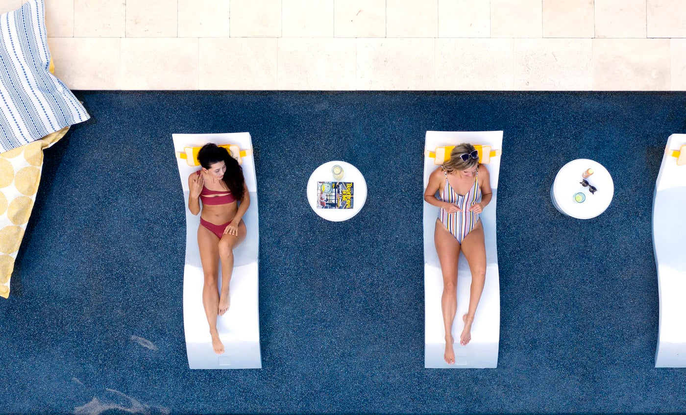Two women lounging on in pool chaises with matching headrest pillows.