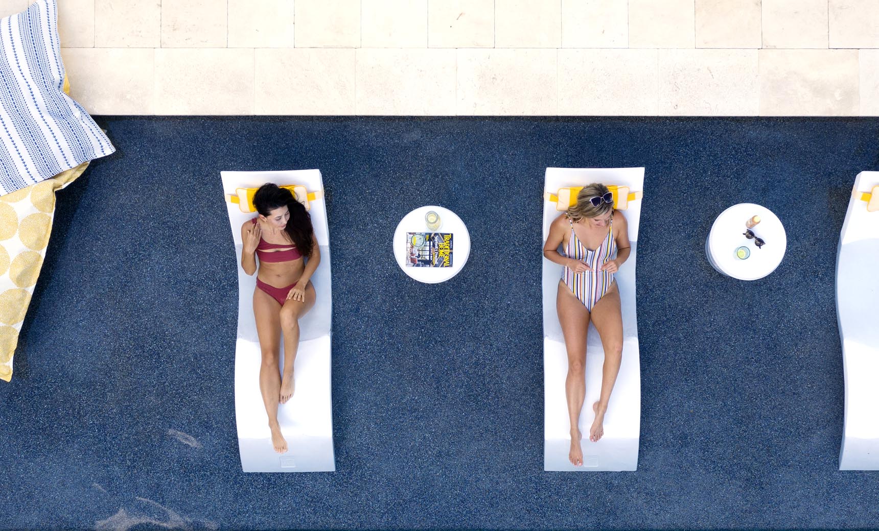 Two women lounging on in pool chaises with matching headrest pillows.