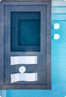 A top-down view of a rectangular grey box with an empty compartment, two white straps, and a round button, placed on a blue surface next to two small white cubes.