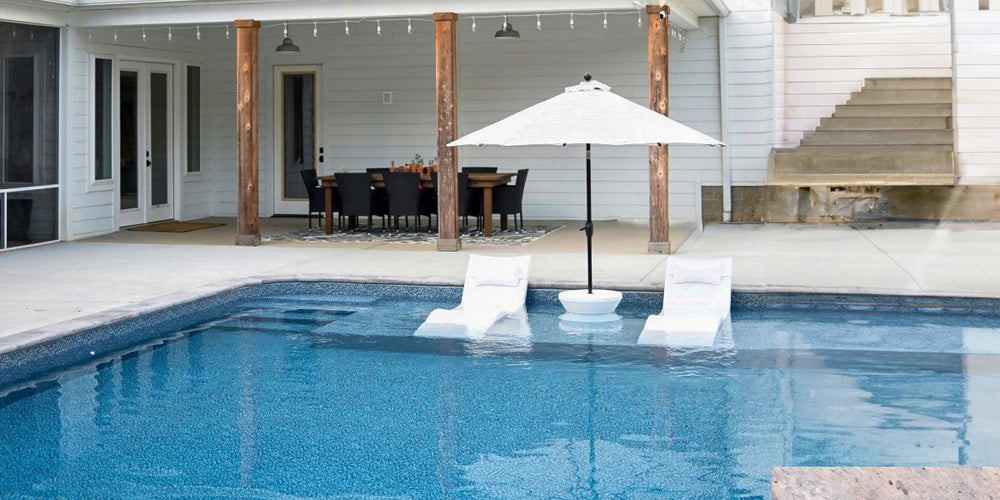 White chaise loungers with white side table and white umbrella on pool ledge