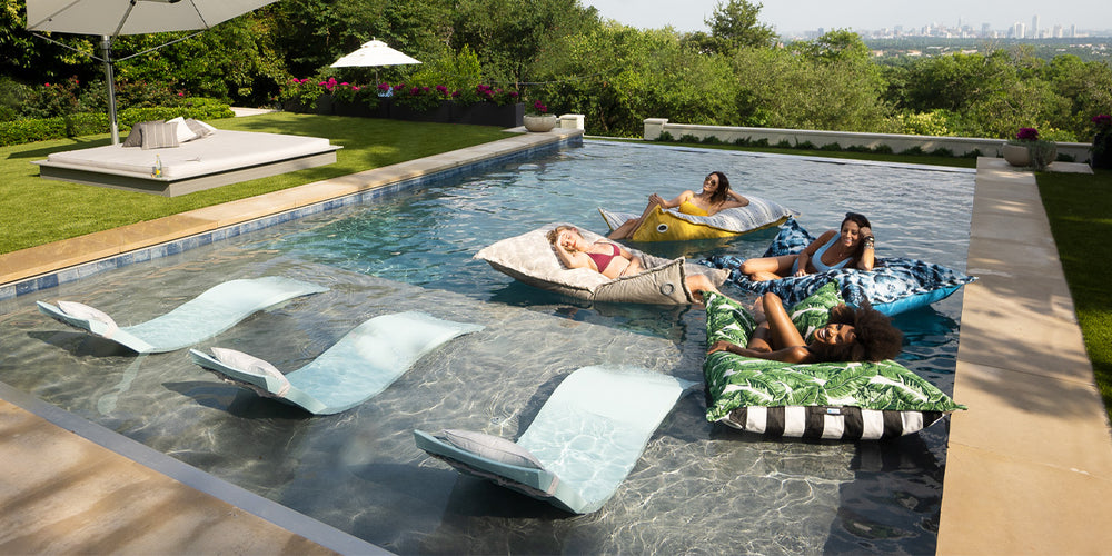 Friends enjoying the summer sun floating on Laze Pillows in the pool