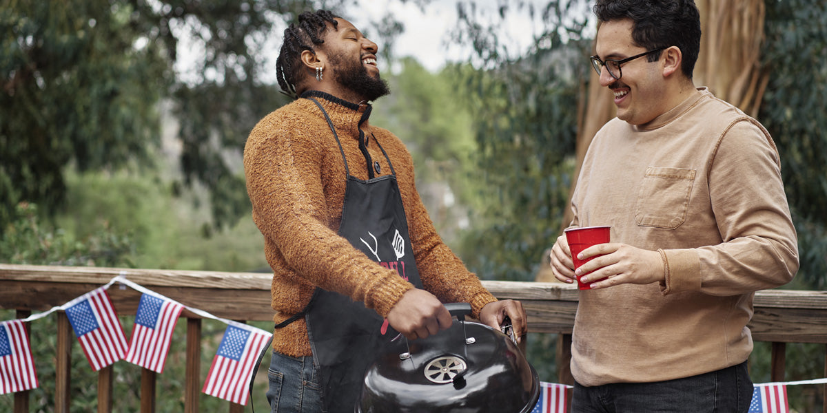 Two men hanging out outside by the grill with small American flags