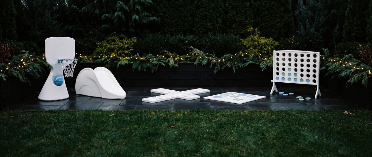 A backyard patio set up with a basketball hoop, a small slide, a giant tic-tac-toe game, and a giant four-in-a-row game.