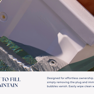 A person submerges the Ledge Lounger Signature Chaise Armrest Console into a pool to fill it with water. Text reads: Easy to fill & maintain—designed for effortless pool ledge use, with straightforward maintenance instructions.