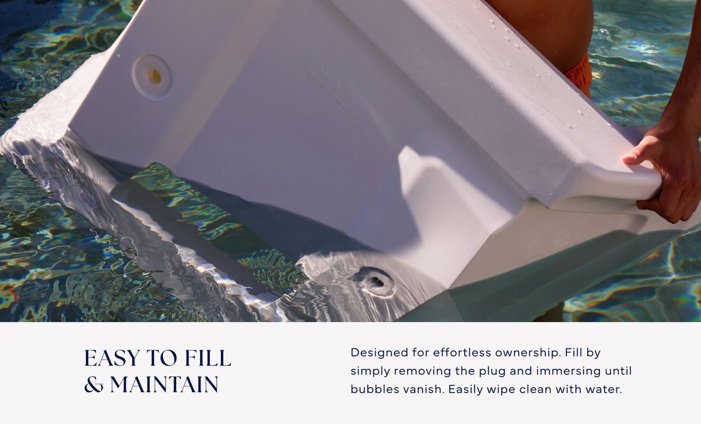 A person submerges the Ledge Lounger Signature Chaise Armrest Console into a pool to fill it with water. Text reads: Easy to fill & maintain—designed for effortless pool ledge use, with straightforward maintenance instructions.