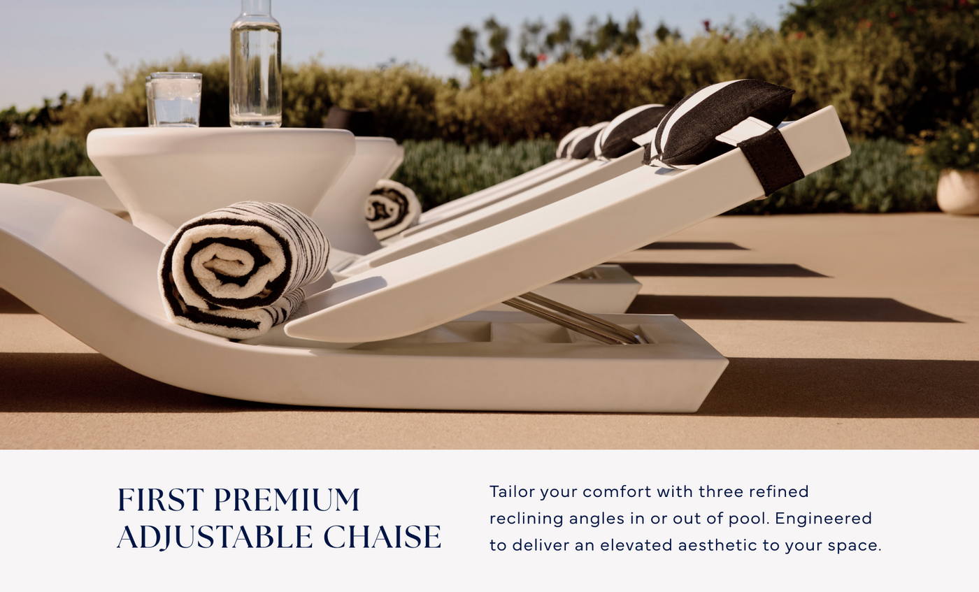 Two Ledge Lounger Signature Adjustable Reclining Chaises with black-and-white rolled towels and a glass bottle sit on a tanning ledge by the pool, surrounded by greenery under a clear sky.