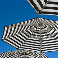 Ledge Lounger’s Signature Chaise and Side Table with Umbrella In-Pool Set features bold black and white stripes—striking geometric canopies set against a bright blue sky, perfect for enhancing your outdoor escape.