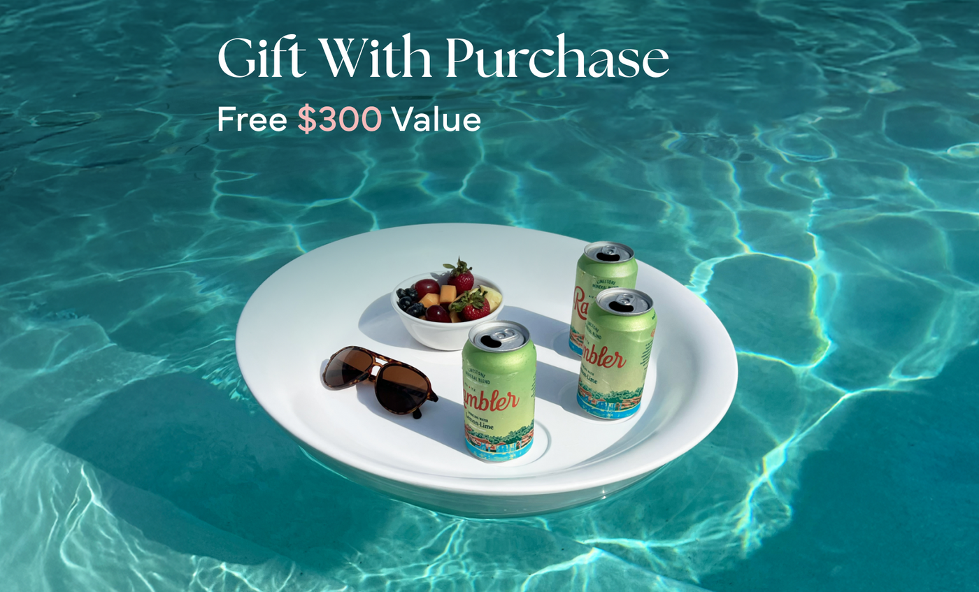 A floating tray in a pool holds Test Product for Transaction Test by Ledge Lounger, berries, and sunglasses. Text above reads Gift With Purchase, Free $300 Value. Sunlight sparkles on the clear blue water.