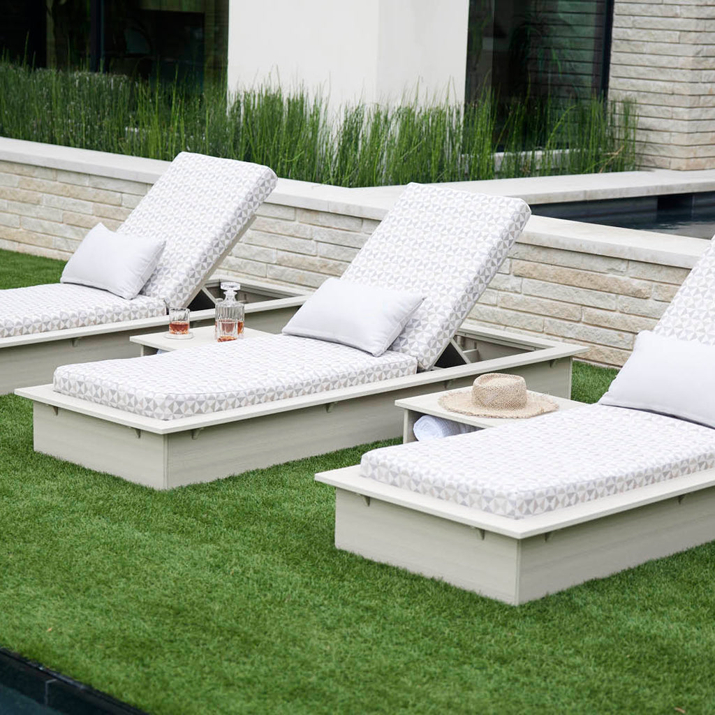 Two white sun loungers on a lawn with white cushions and small side tables