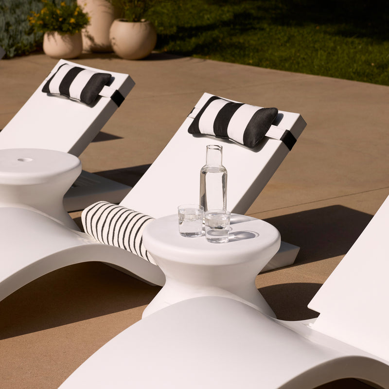 Modern white outdoor lounge chairs with black-and-white striped cushions, set on a patio with a small matching side table holding a glass bottle and two glasses.