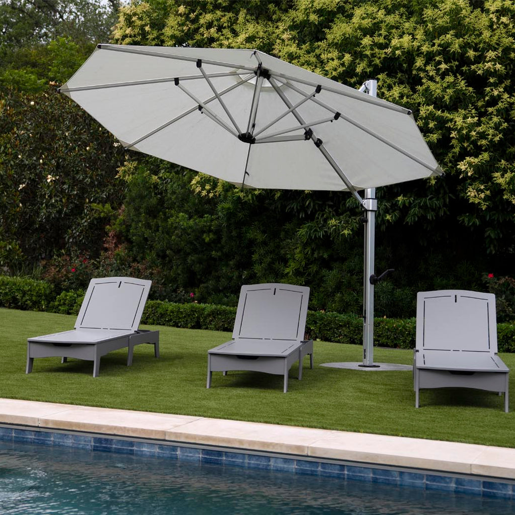 A large patio umbrella with a metal pole and four gray chaise lounges placed on artificial grass.