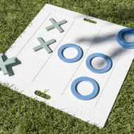 The Ledge Lounger Oversized Patio Games Set features a large white tic-tac-toe board with blue Os and green Xs on green grass. Three Os form a winning line in the center row, making this outdoor game set perfect for backyard fun.