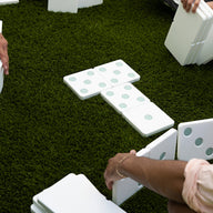 Several people play with the Ledge Lounger Oversized Patio Games Set on green grass, arranging the large white tiles—an ideal backyard game for family fun.
