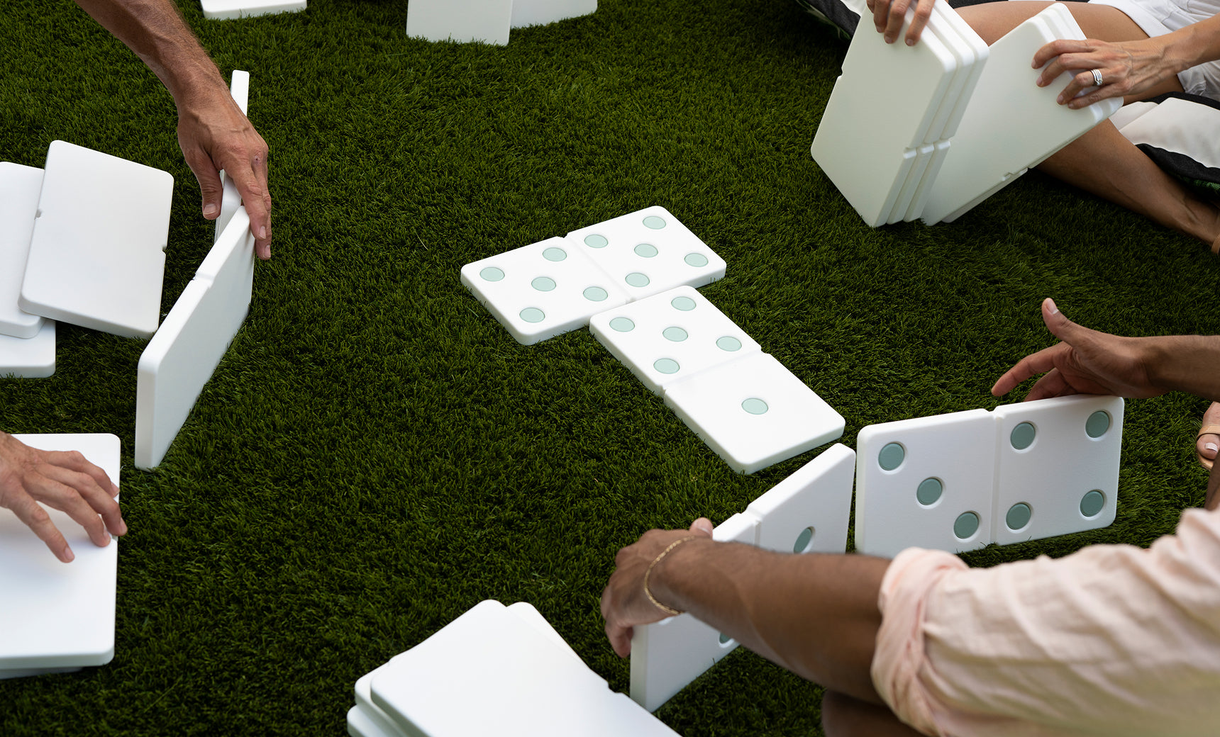 Several people play with the Ledge Lounger Oversized Patio Games Set on green grass, arranging the large white tiles—an ideal backyard game for family fun.