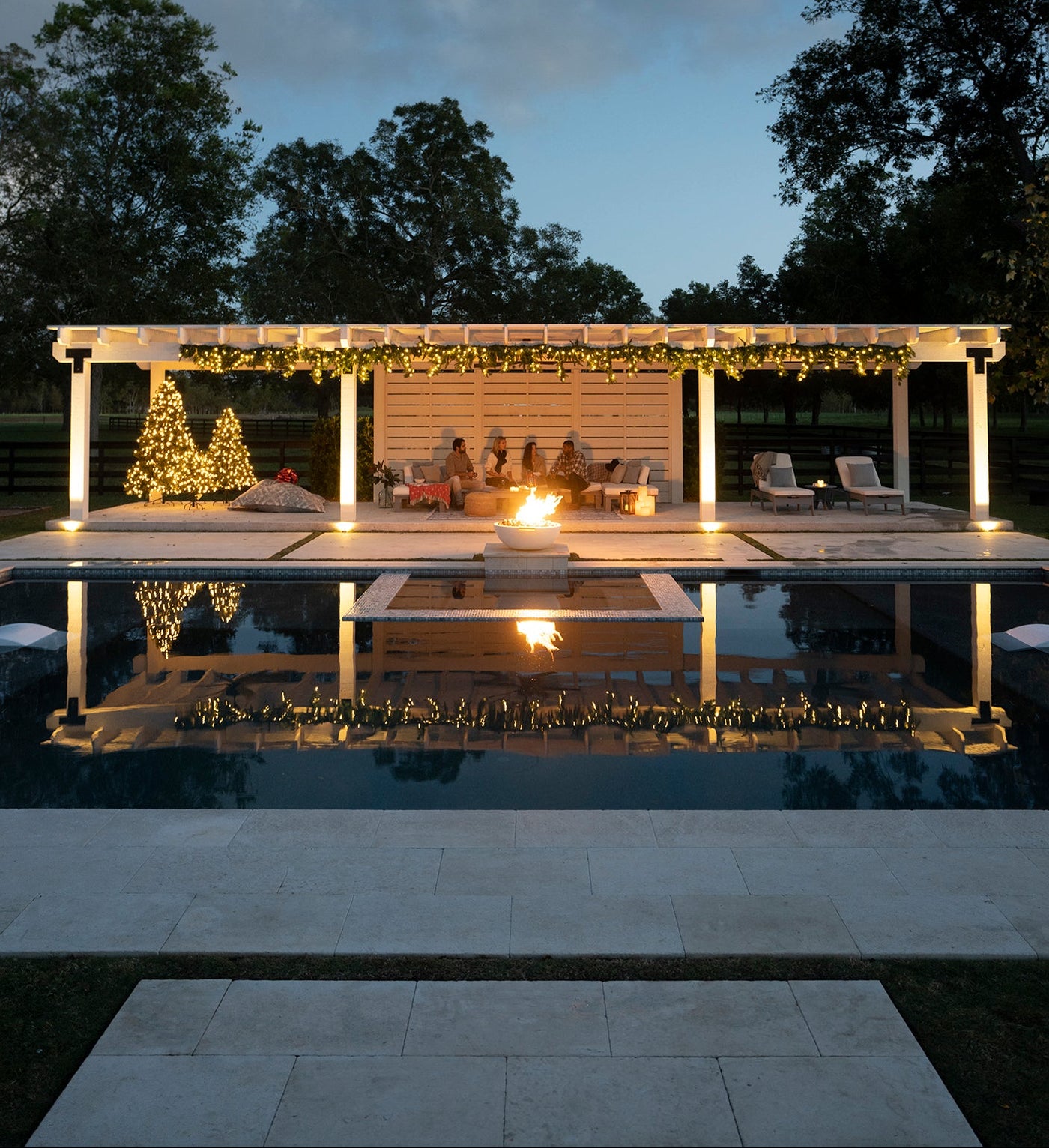 Garden with pool, pergola, and Christmas decorations at dusk.